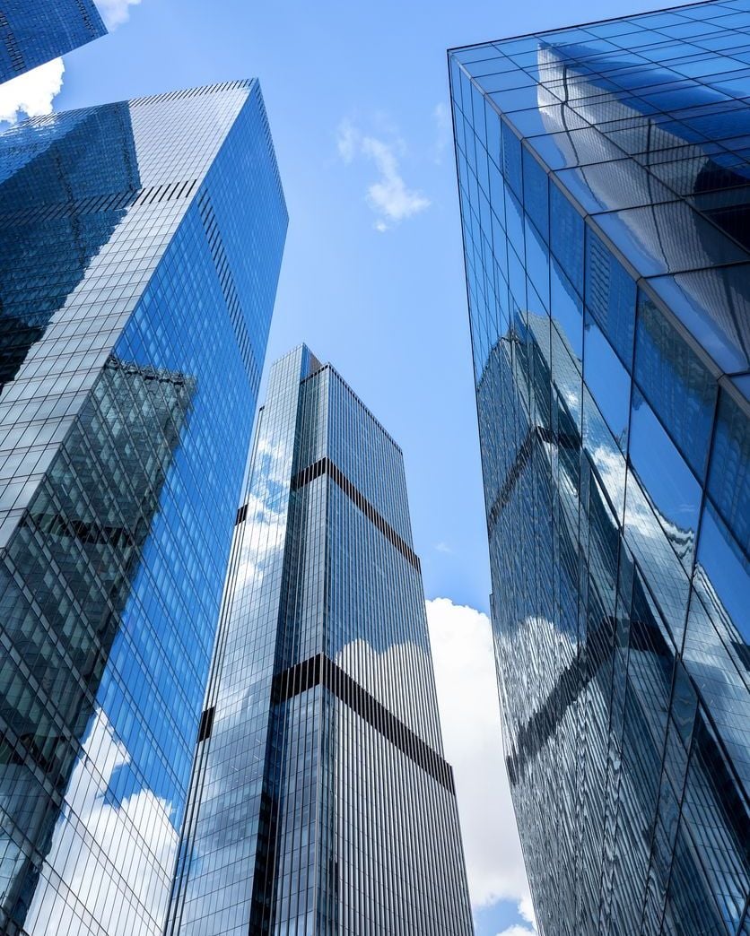 Low-angle view oftowering modern glass skyscrapers reflecting blue sky and white clouds.