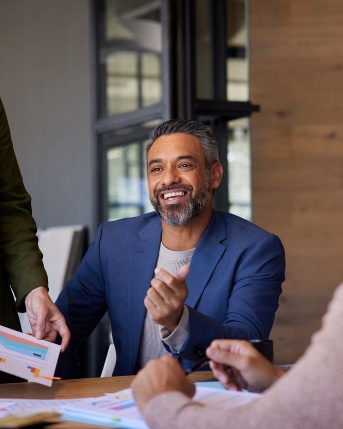 Smiling mid adult indian businessman sharing ideas during a meeting. Engaged team members in a collaborative discussion. Positive business meeting with teamwork and strategy planning.